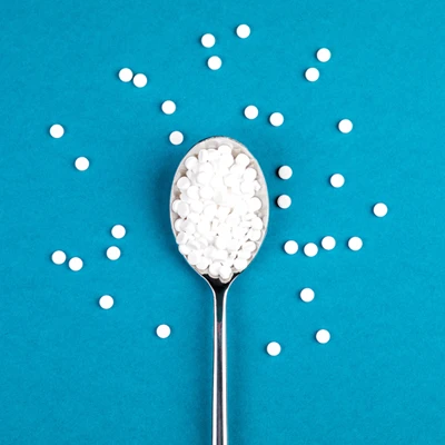 Löffel mit weißen Süßstofftabletten auf blauem Hintergrund, weitere Tabletten rundherum verteilt