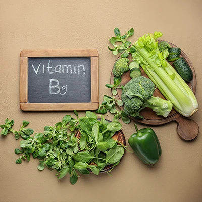 Green vegetables beside chalkboard reading “Vitamin B9” – natural display of folate-rich foods