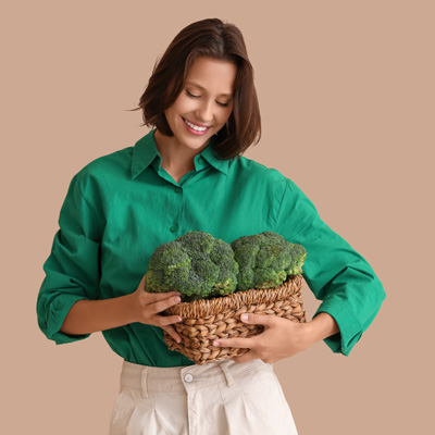 Frau in grünem Hemd hält Korb mit frischem Brokkoli – gleichmäßiges Studiolicht, natürliche und gesunde Bildwirkung