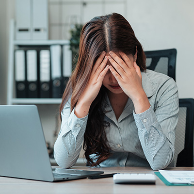 Frau sitzt erschöpft am Schreibtisch vor Laptop – Symbol für mentale Belastung und Konzentration