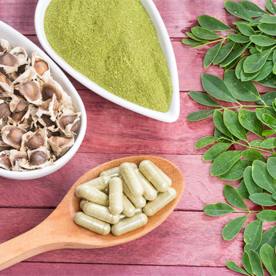 Moringa-Pulver, Kapseln und Blätter auf rosa Holzfläche – natürliche Nahrungsergänzung