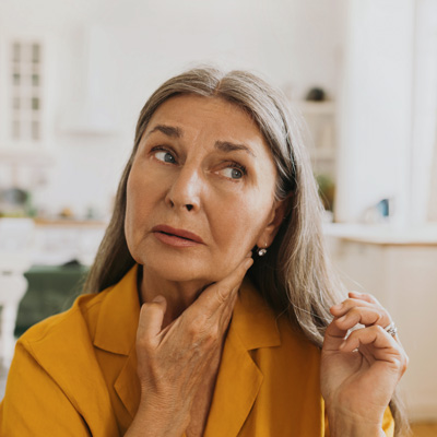 Older woman touching her neck and looking thoughtfully to the side – bright daylight, symbol of thyroid concerns