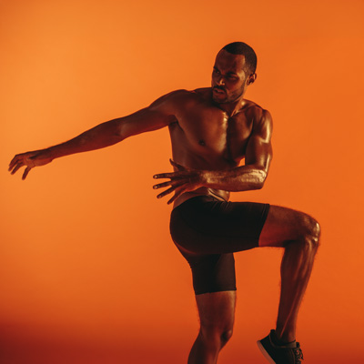 Sportler wärmt sich vor orangefarbenem Hintergrund dynamisch auf – kraftvolle Fitnessaufnahme