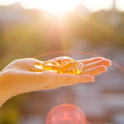 Hand holding yellow capsules in sunlight outdoors – warm light, clear and vivid presentation