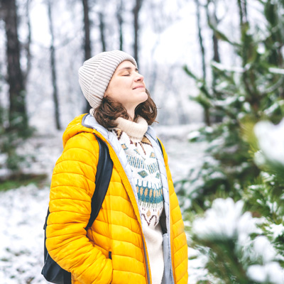 Woman in yellow jacket enjoying winter air with closed eyes in snowy forest – bright daylight, fresh atmosphere