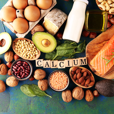 Verschiedene Lebensmittel mit Buchstabenwürfeln „Calcium“ – bunte Auswahl aus Nüssen, Linsen, Avocado, Fisch und Milchprodukten