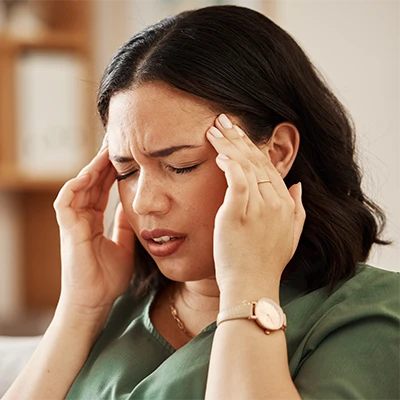Woman holding both hands to her temples and appearing tense – soft daylight indoors