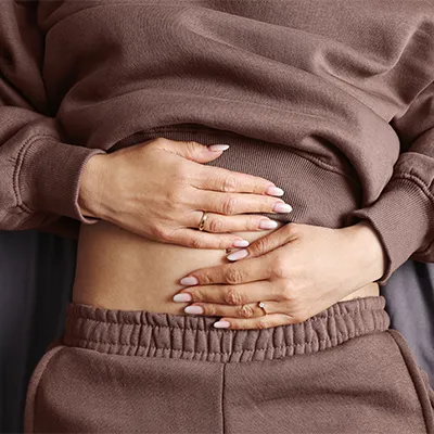 Person hält beide Hände auf den Bauch – Nahaufnahme in brauner Freizeitkleidung