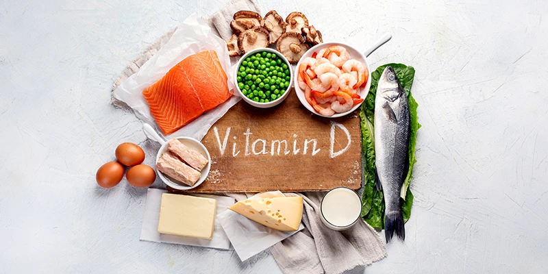 Vitamin-D-Lebensmittel mit Lachs, Fisch, Eiern, Käse, Milch, Pilzen, Erbsen und Garnelen auf hellem Untergrund