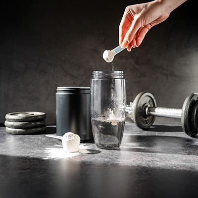 Scoop of L-arginine powder above a shaker, with dumbbell and weights – athletic training setting