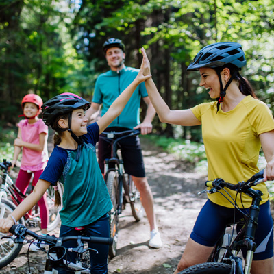 Family with bicycles on a forest trail, mother and child high-five – sunny daylight, active outdoor recreation