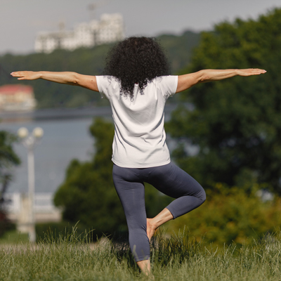 Frau macht Yoga im Freien im Baum-Stand – Symbol für Gleichgewicht, Durchblutung und ganzheitliche Gesundheit
