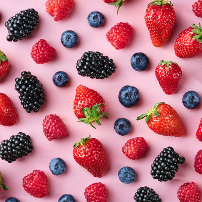 Beerenstark durch den Sommer - mit Antioxidantien & Vitamin C Erdbeeren, Himbeeren, Brombeeren und Blaubeeren auf rosa Hintergrund – Symbol für Antioxidantien und Sommerenergie