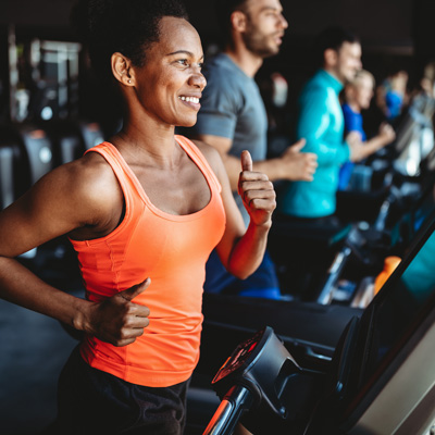 Woman running on a treadmill at the gym, other exercisers in the background – modern fitness environment