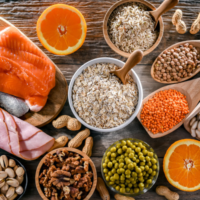 Vitamin-B1-reiche Lebensmittel wie Lachs, Haferflocken, Linsen, Nüsse und Orangen auf Holztisch