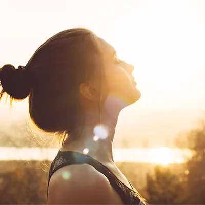 Woman with tied-back hair enjoying warm evening sunlight outdoors – calm atmosphere, symbol of well-being