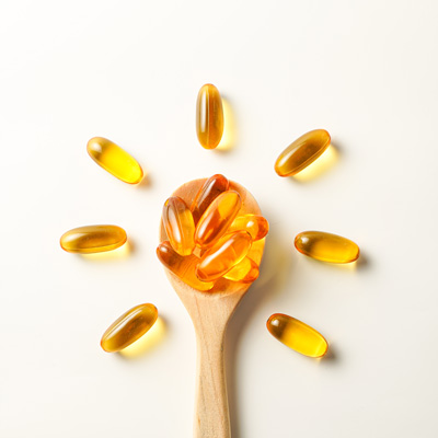 Goldene Kapseln auf Holzlöffel vor hellem Hintergrund – gleichmäßiges Licht, klare und reduzierte Darstellung 