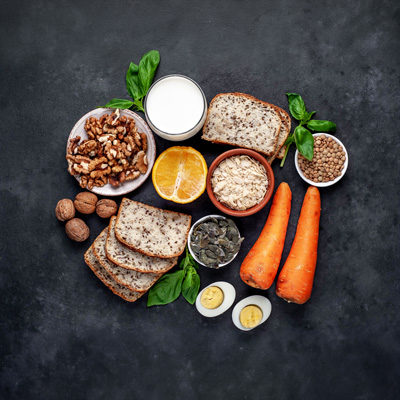 Vitamin-B1-reiche Lebensmittel mit Nüssen, Vollkornbrot, Linsen und Karotten auf dunklem Hintergrund