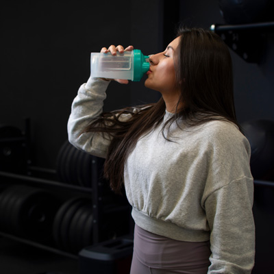 Frau trinkt aus Shaker im Fitnessstudio – ruhige Szene nach dem Training