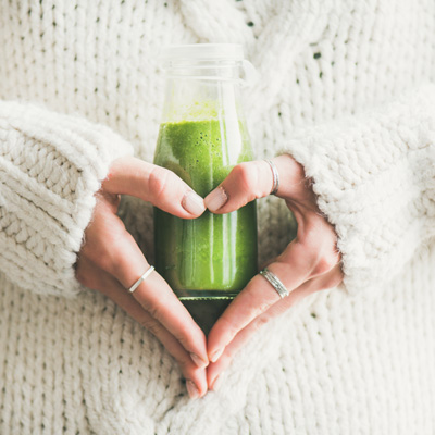 Hände halten grünen Smoothie in einer Glasflasche – helle Kleidung und natürliche Bildwirkung