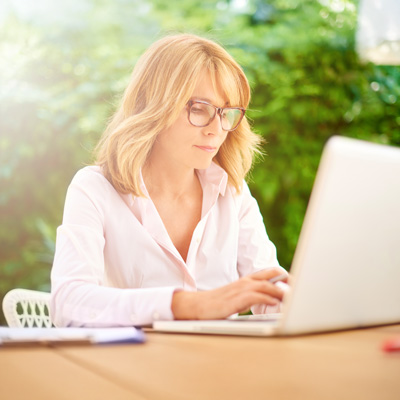 Woman with glasses working on laptop outdoors – symbol of focus, self-care and flexible summer work