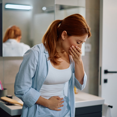 Pregnant woman holding her stomach and mouth in bathroom – soft lighting, calm everyday scene with nausea