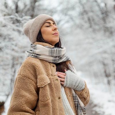 Woman in winter coat taking a deep breath while walking through snowy forest