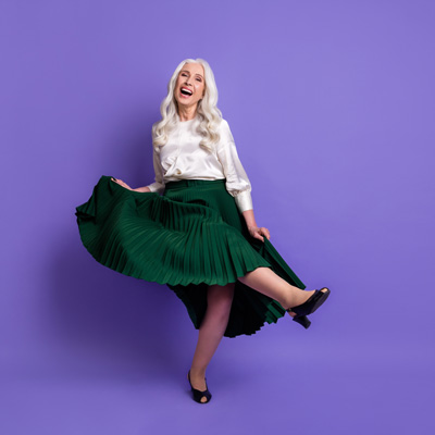 Fröhliche Frau in grünem Rock tanzt vor violettem Hintergrund – gleichmäßiges Studiolicht, lebendige und beschwingte Stimmung