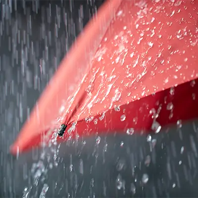 Red umbrella in heavy rain with visible water droplets – dark, wet weather atmosphere