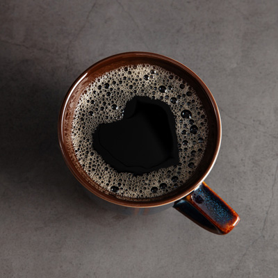 Tasse mit schwarzem Kaffee und feiner Crema auf grauer Oberfläche – dunkle, ruhige Bildstimmung