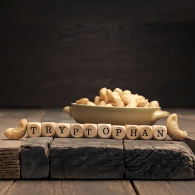 Wooden letter blocks spelling “Tryptophan” in front of a bowl of cashew nuts on a rustic wooden table