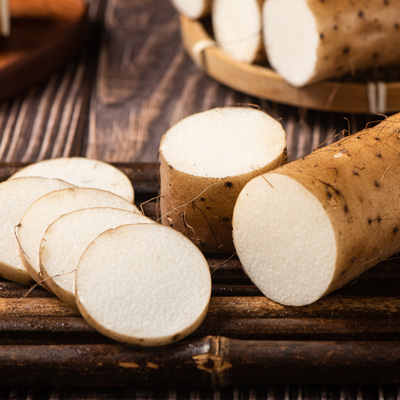 Aufgeschnittene Yamswurzel und mehrere Scheiben auf dunklem Holztisch – warme, natürliche Bildwirkung