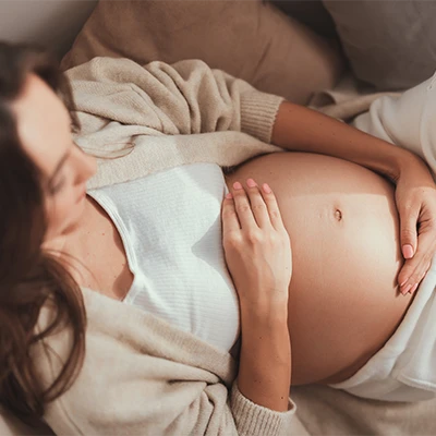 Pregnant woman lying relaxed with hands on her belly – soft, warm indoor light