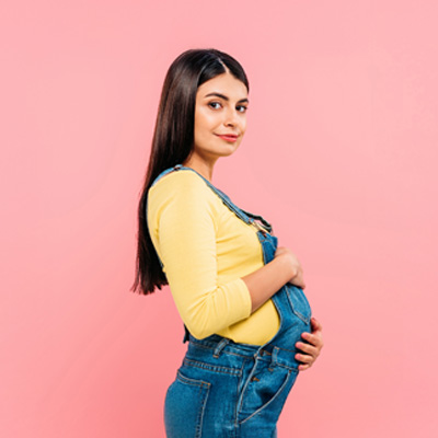 Small strength for big changes “Pregnant woman in overalls against pink background – symbol of pregnancy, nutrient support and women’s health”