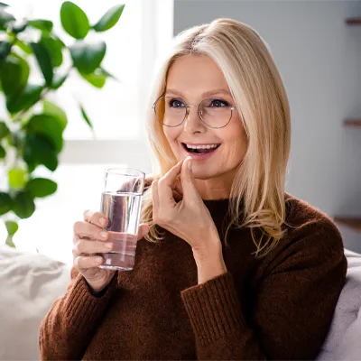 Lächelnde Frau nimmt eine Kapsel ein und hält ein Glas Wasser – helles Tageslicht