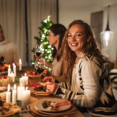 Junge Frau lacht bei festlichem Abendessen im Kerzenschein – gemütliche Weihnachtsstimmung mit gedecktem Tisch im Hintergrund
