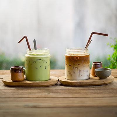 Two iced matcha and coffee drinks in glasses with straws on a wooden table – soft daylight