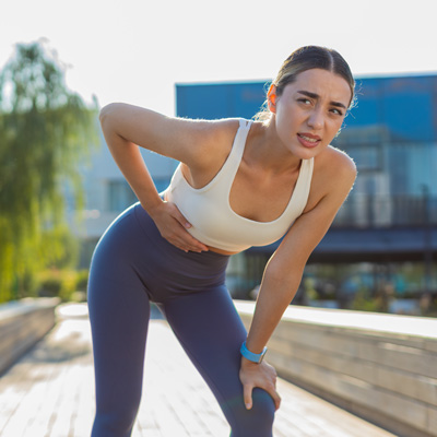 Sportlerin hält sich beim Training seitlich den Bauch – helles Tageslicht im Freien