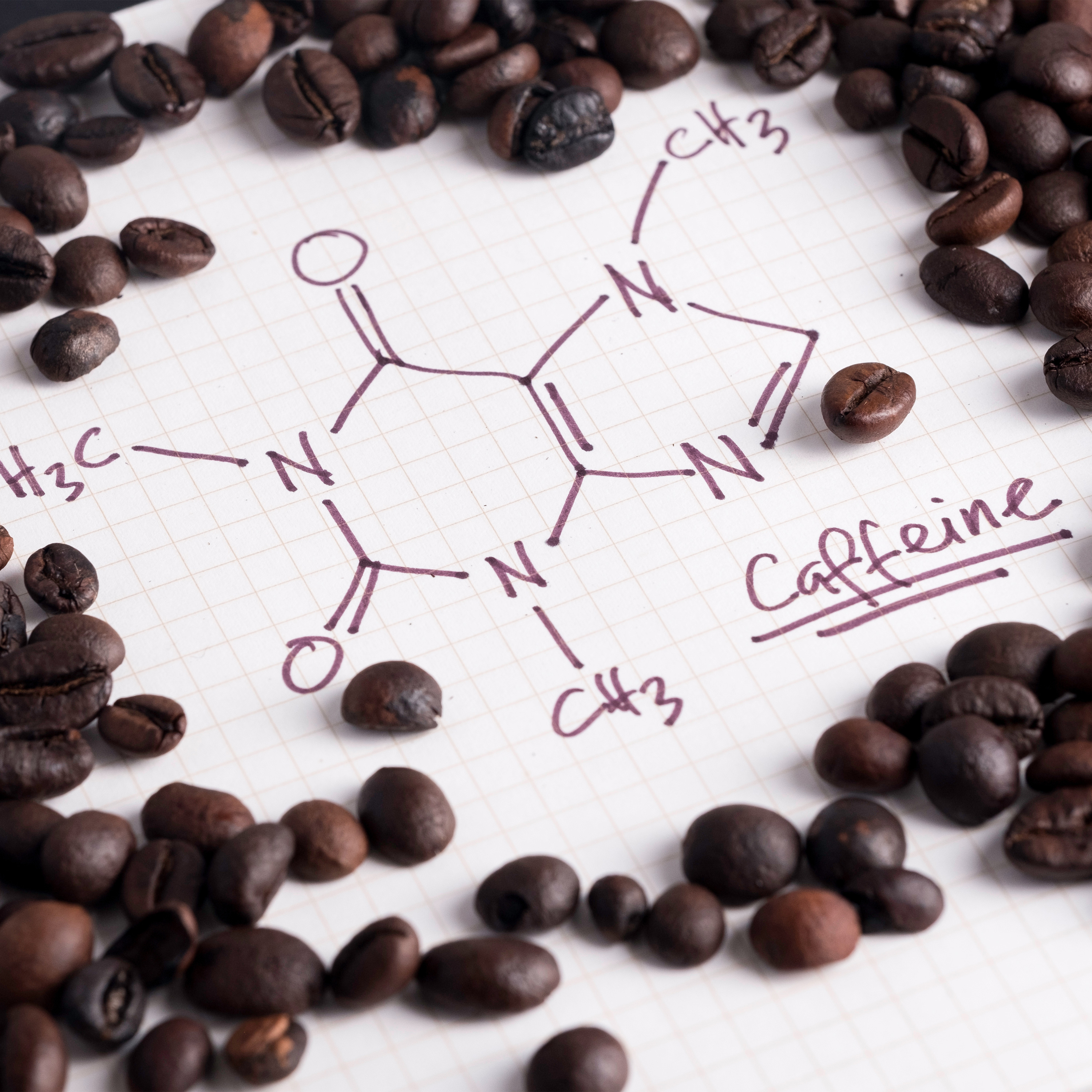 Drawn caffeine structural formula on paper framed by coffee beans – scientific close-up