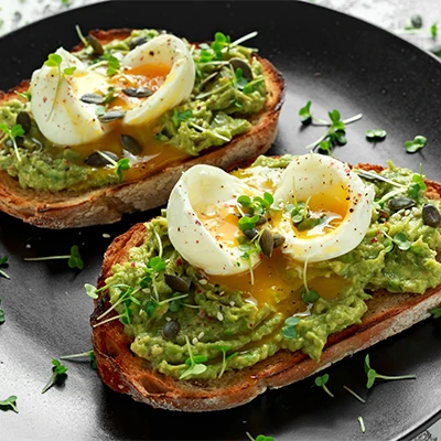Avocado-Toast mit Eiern, Sprossen und Kernen auf schwarzem Teller – appetitliche Nahaufnahme