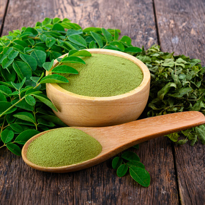 Moringa-Pulver in Holzschale mit frischen und getrockneten Blättern auf rustikalem Holz