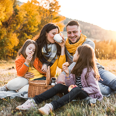 Familie picknickt auf einer Wiese im goldenen Herbstlicht – warme Abendsonne, bunte Blätter, entspannte Stimmung