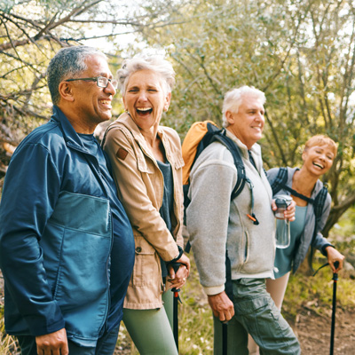Gruppe älterer Menschen wandert lachend durch sonnigen Wald – warmes Tageslicht, aktive und fröhliche Naturstimmung
