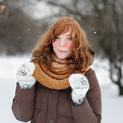 Young woman with rosy cheeks in snowfall, warmly dressed with scarf and gloves – soft winter light, fresh atmosphere