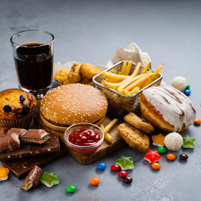 Fast Food, Süßigkeiten und Cola auf grauem Tisch – mögliche Auslöser für Sodbrennen