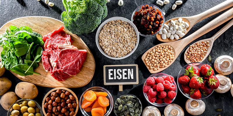 Eisenreiche Lebensmittel wie Fleisch, Spinat, Hülsenfrüchte und Haferflocken rund um Schild „Eisen“