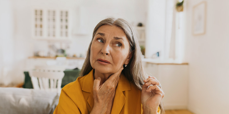 Older woman touching her neck and looking thoughtfully to the side – bright daylight, symbol of thyroid concerns