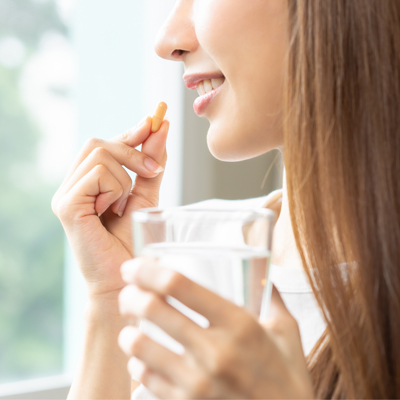 Smiling woman taking a capsule with a glass of water – soft daylight, calm atmosphere