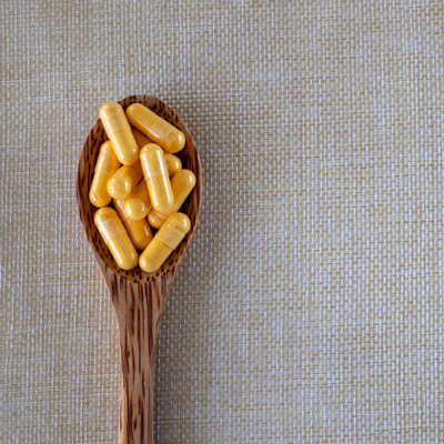 Yellow capsules in wooden spoon on light fabric background – soft lighting, minimalist product presentation 