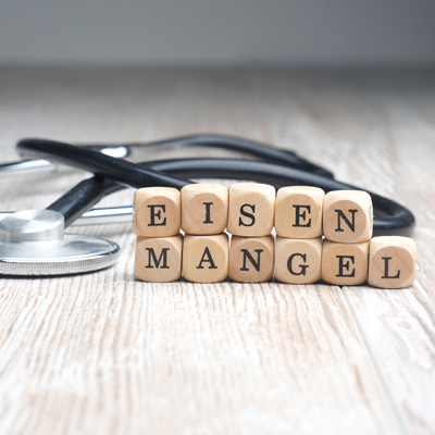 Cubes spelling “Eisenmangel” in front of a stethoscope on wooden surface